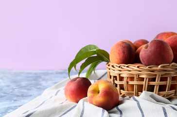 Wicker basket of fresh peaches on table against lilac background