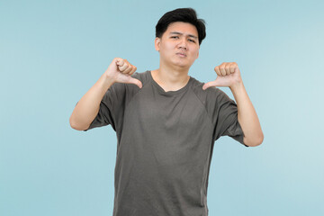 young asian man giving thumbs down showing disagree or dislike in studio background