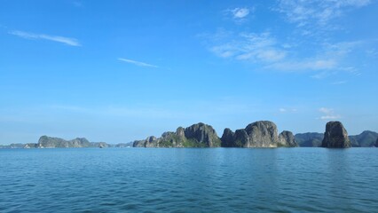 A scenic view of calm emerald waters with limestone islets in Ha Long Bay, Vietnam, under a clear blue sky.
