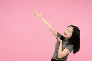 short asian woman pointing and looking up on pink studio background