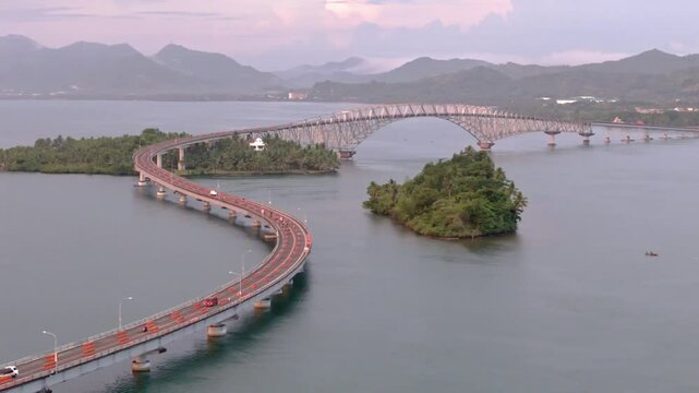 Drone semi orbit of the San Juanico Bridge at sunset. Smooth traffic over the winding structure above blue water and islands.