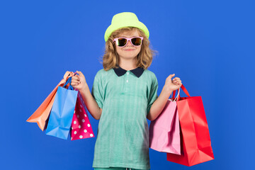 Kid boy in fashion clothes goes shopping. Kid with shopping packages. Shopper child with carrying...