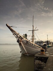 A phinisi ship sits calmly at a pier under a serene sky, bathed in soft, diffused light.