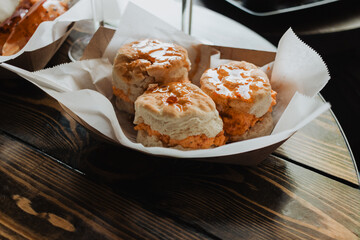 Three glazed pimento cheese biscuit sandwiches served in a paper-lined tray on a rustic wooden table