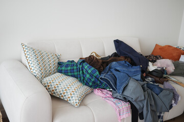 Cluttered couch with piles of clothes and cushions