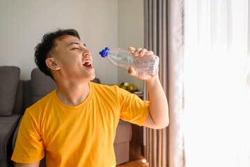 Indonesian southeast asian man drinking water after finishing a home body workout exercise session for a fit physique and a healthy sport lifestyle at home. Fitness and active lifestyles concept