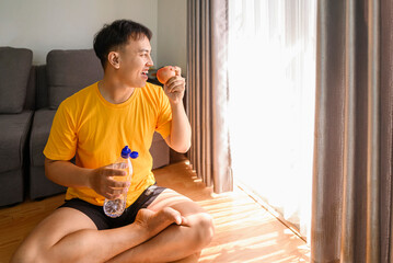 Indonesian southeast asian man drinking water and eating fruit after finishing a home body workout exercise session for a fit physique and healthy sport at home. Fitness and active lifestyles concept