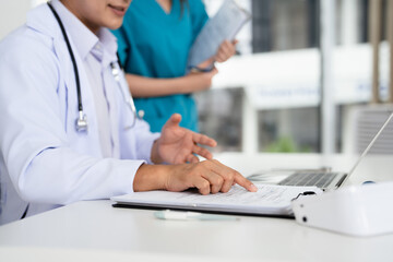 Doctors and nurse looking at clipboard, discussing patient's illnesses or diagnosis in clinic.