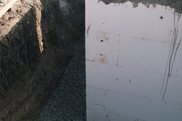 Excavated trench beside an insulated concrete wall during pool construction. The wall is covered...