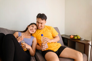 Indonesian southeast asian couple drinking water after finishing a home body workout exercise session for a fit physique and a healthy sport lifestyle at home. Fitness and active lifestyles concept