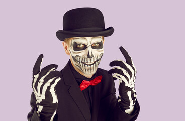 Portrait of young man with scary skull makeup. Spooky man wearing black bowler hat and red bow tie gesturing over isolated studio background. Day of the Dead, Halloween concept