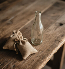 Two burlap bags and a glass bottle sit on a rustic wooden table