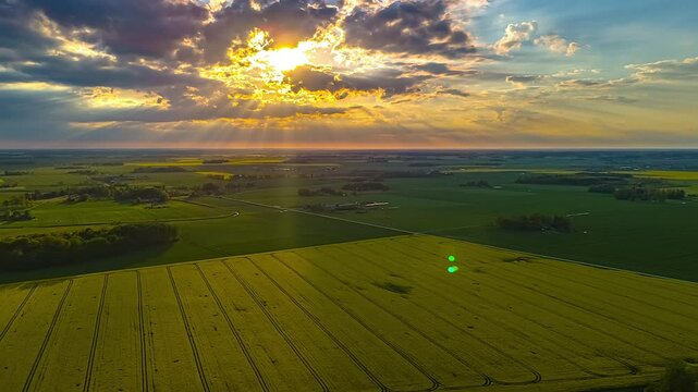 Sunbeams breaking through dramatic clouds above patchy yellow fields at sunset hyperlapse