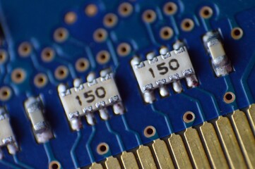 A macro photograph of a blue circuit board featuring white resistors labeled 