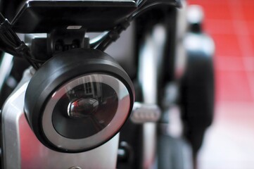A close-up image of a modern motorcycle headlight, focusing on the circular lens and sleek design