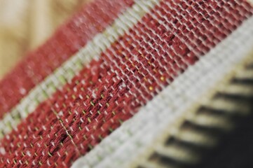 A macro shot of a woven textile, showcasing the intricate details of red and white yarn threads...