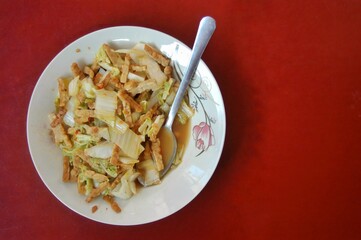 A top view of a plate of stir-fried cabbage and tempeh served with a spoon