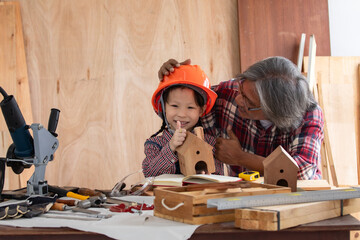 Asia retirement carpenter man spends time with cheerful granddaughter in carpentry studio, aged...