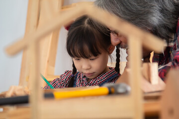 Asia retirement carpenter man spends time with cheerful granddaughter in carpentry studio, aged...