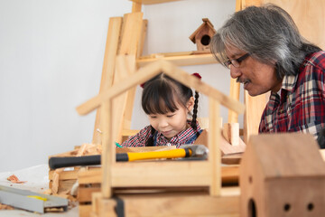 Asia retirement carpenter man spends time with cheerful granddaughter in carpentry studio, aged...