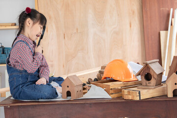 a curious Asian girl uses a magnifying glass to inspect a wooden object in a carpentry area,...