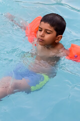 Happy Indian boy swimming in a pool, Kid wearing swimming costume along with air tube during hot...