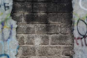 a weathered concrete wall with exposed brick and faded graffiti, featuring rough textures and an...