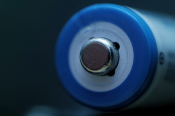 Close-up of the positive terminal of a blue cylindrical battery, highlighting the metallic contact...