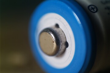 Close-up of a blue cylindrical battery's positive terminal, showing metallic contact points and slight surface wear