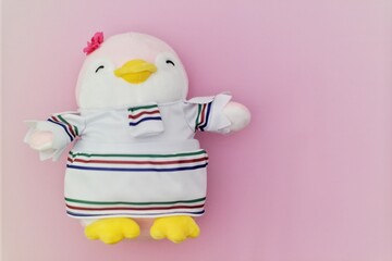 A pink penguin plush toy wearing a striped outfit and a small flower accessory, positioned against...