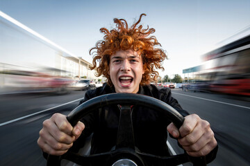 A red-haired guy holds the steering wheel of a car in front of him and rushes along the highway.