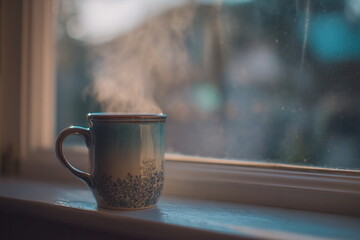 A steaming ceramic mug placed by the window, capturing the cozy warmth of a quiet morning and the calm simplicity of home comfort in natural light