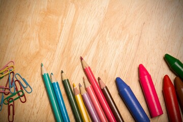 Coloring tools are lying on flat design wooden table with colored pencils, crayons, paper clips