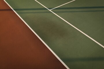Flat-design court surface is showing brownish-red joining green with white lines and fence shadows
