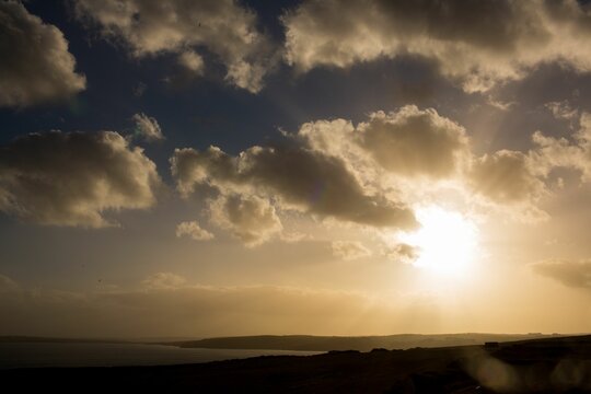Fototapeta Golden sun is shining through scattered cumulus clouds over calm bay with headland in flat design