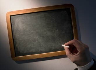 Hand holding chalk over chalkboard