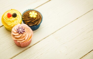 Three swirl frosting cupcakes with candy toppers are sitting on wooden plank in flat design