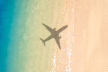 Aerial view of shadow passenger plane silhouette and sandy beach blue sea with waves at sea beach...