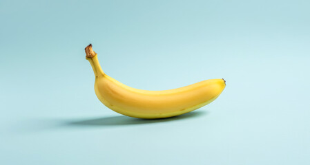 Single yellow banana isolated on a light blue background.