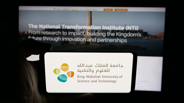 Stuttgart, Germany - 06-14-2025: Person holding cellphone with logo of Saudi King Abdullah University (KAUST) on screen in front of webpage. Focus on phone display.