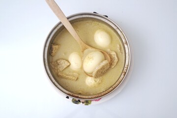 Top-down view of a pot of Opor Telur, a traditional Indonesian dish with eggs and tempeh in a creamy coconut milk broth. The light composition emphasizes the simplicity and warmth of homemade cooking.