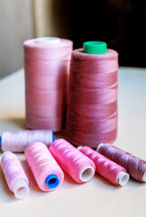 Colorful pink tailoring threads close-up on wooden background.