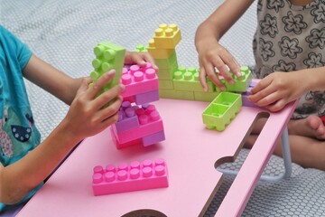 Two children are playing with brightly colored building blocks on a pink table