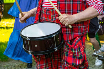 Clown in a red tartan costume playing a snare drum during an outdoor street performance. Colorful...