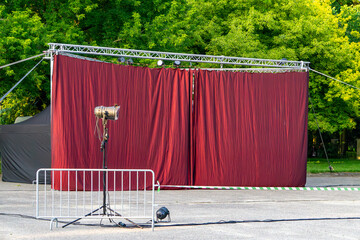 Outdoor theater stage with a red curtain, spotlight, and metal barrier, set against a backdrop of...