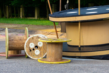 Wooden cable reels placed on asphalt outdoors, next to a large decorative element. Industrial theme...