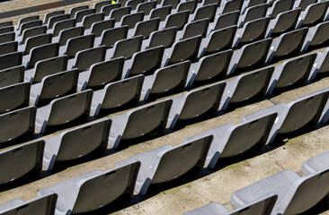 Fototapeta premium Rows of empty plastic stadium seats forming a geometric pattern. Symmetrical layout in natural sunlight, typical for sports arenas or outdoor event venues.