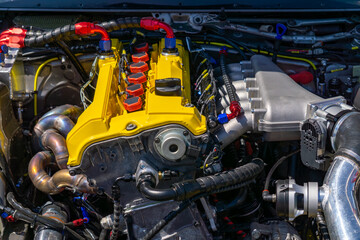 modified car engine with a yellow valve cover, colorful wiring, and visible tuning components in a clean engine bay