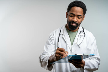 Smiling black doctor writing notes on clipboard, studio isolated portrait