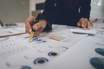 A businesswoman analyzes financial documents with charts and graphs at a desk, highlighting data...
